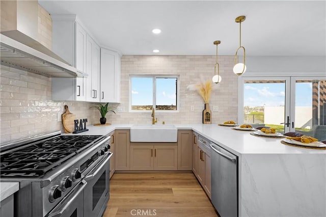 kitchen with wall chimney exhaust hood, light countertops, a sink, and appliances with stainless steel finishes