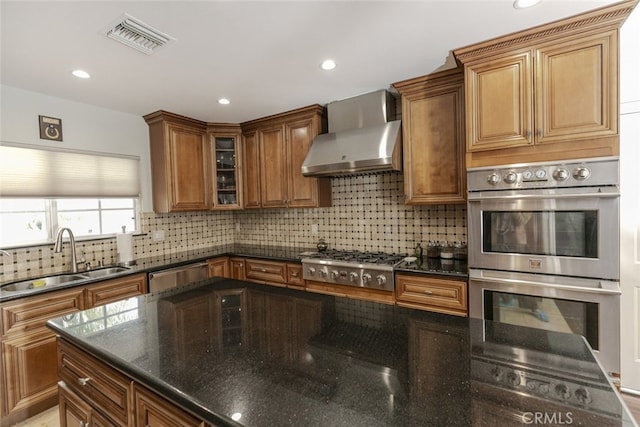 kitchen with visible vents, appliances with stainless steel finishes, a sink, dark stone counters, and wall chimney exhaust hood
