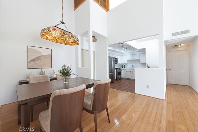 dining space featuring light wood-type flooring, visible vents, and a high ceiling