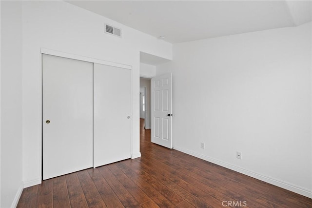 unfurnished bedroom featuring wood-type flooring, baseboards, visible vents, and a closet