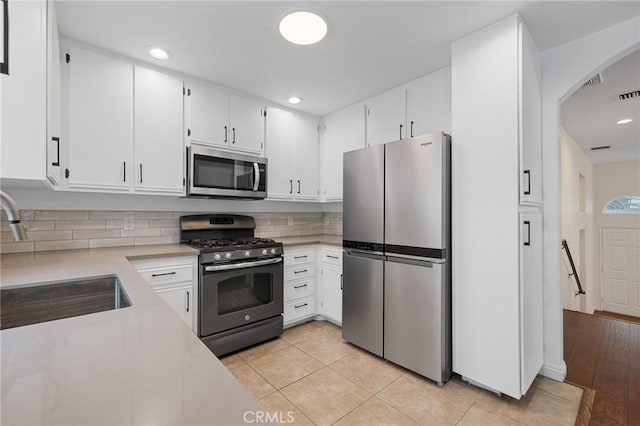 kitchen featuring white cabinets, arched walkways, a sink, light countertops, and appliances with stainless steel finishes