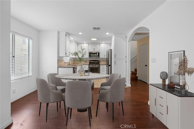 dining area featuring visible vents, arched walkways, dark wood-style floors, and baseboards