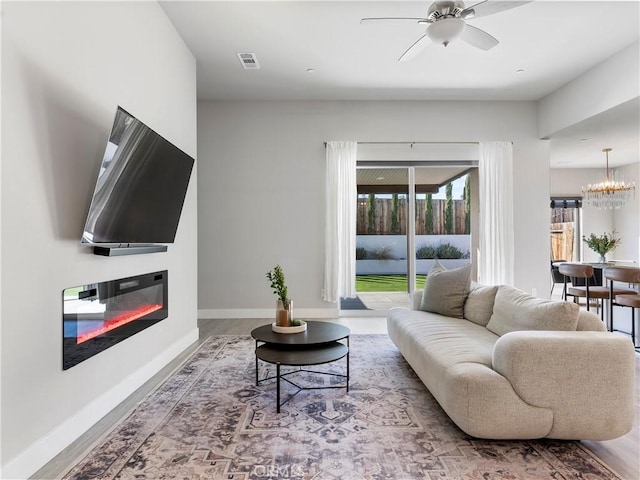 5211 Wingspan Ln, Bakersfield, CA 93306 - living area featuring a glass covered fireplace, visible vents, baseboards, wood finished floors, and ceiling fan with notable chandelier