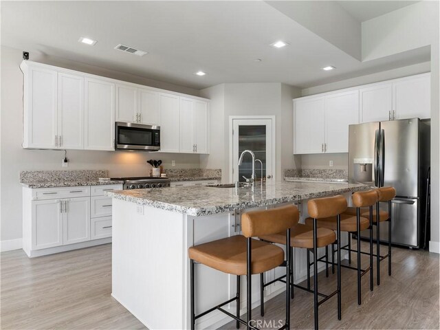 5211 Wingspan Ln, Bakersfield, CA 93306 - kitchen with a sink, light wood-type flooring, a center island with sink, visible vents, and appliances with stainless steel finishes