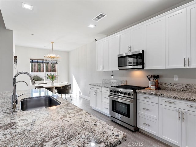 5211 Wingspan Ln, Bakersfield, CA 93306 - kitchen with an inviting chandelier, stainless steel appliances, light wood finished floors, a sink, and visible vents