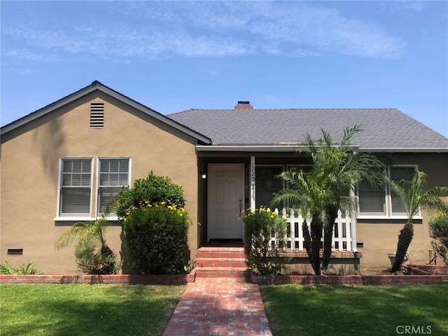 view of front facade with roof with shingles, stucco siding, a chimney, and a front yard