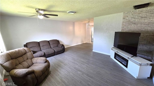 living area with a fireplace, a textured ceiling, a ceiling fan, and dark wood-type flooring