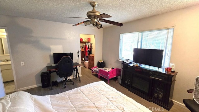 bedroom with a textured ceiling, a spacious closet, wood finished floors, a closet, and ceiling fan