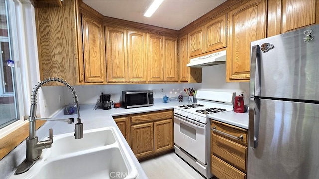 kitchen with a sink, freestanding refrigerator, white range with gas cooktop, brown cabinets, and under cabinet range hood