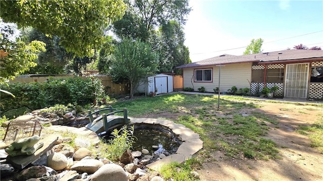 view of yard with a small pond, fence, an outbuilding, and a storage unit