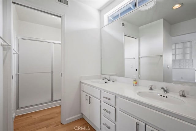 bathroom with a shower stall, wood finished floors, double vanity, and recessed lighting