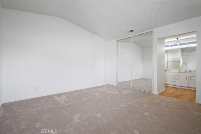 unfurnished bedroom with carpet floors, lofted ceiling, a closet, and ensuite bath