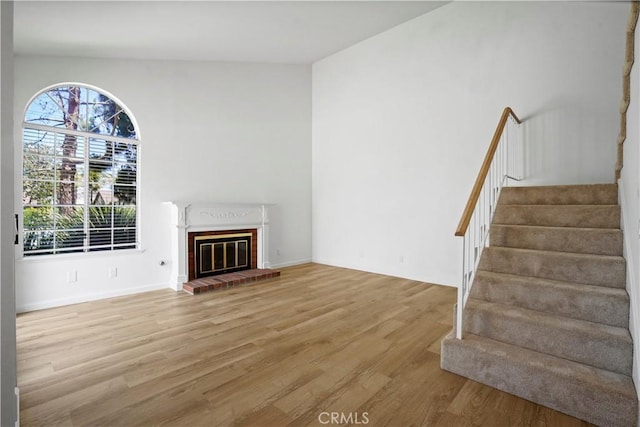 unfurnished living room featuring wood finished floors, stairs, and a fireplace