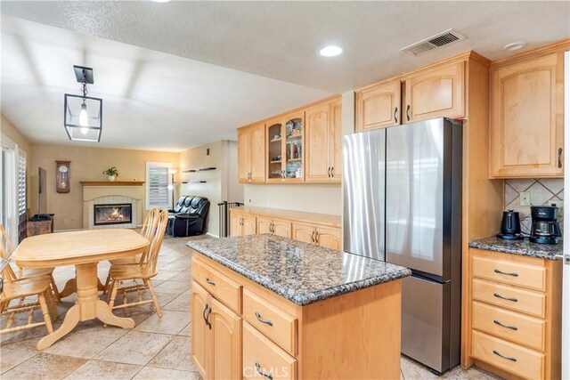 kitchen with a kitchen island, visible vents, freestanding refrigerator, dark stone counters, and light brown cabinets
