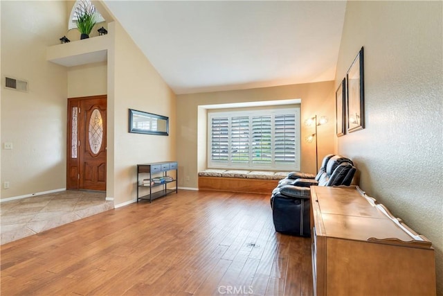 sitting room with visible vents, light wood-style flooring, baseboards, and high vaulted ceiling
