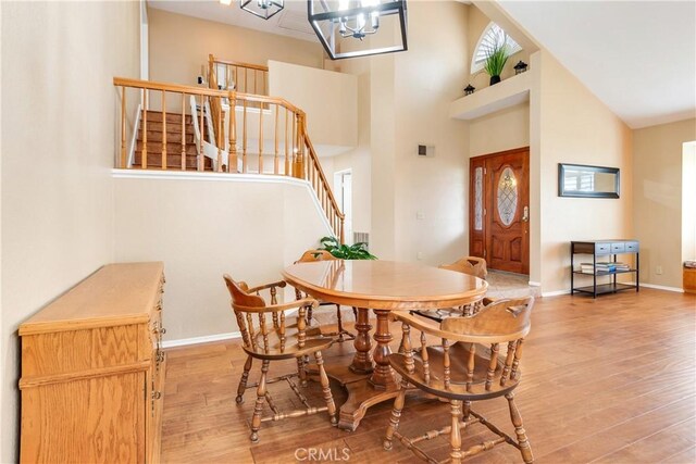 dining room with light wood-type flooring, stairs, visible vents, and high vaulted ceiling