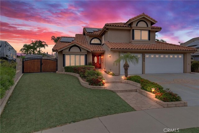 mediterranean / spanish-style house with driveway, a tile roof, a gate, roof mounted solar panels, and stucco siding