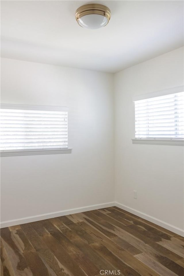 spare room featuring baseboards and dark wood-style floors