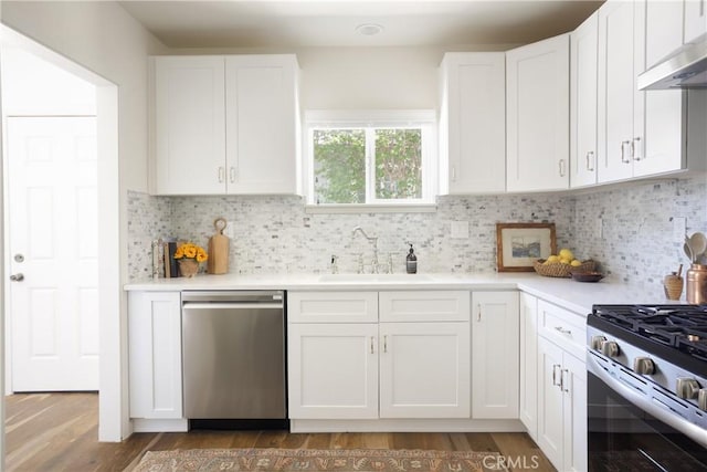 kitchen with appliances with stainless steel finishes, a sink, light countertops, under cabinet range hood, and white cabinetry