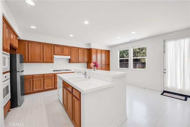 kitchen with recessed lighting, white appliances, light countertops, brown cabinets, and a sink