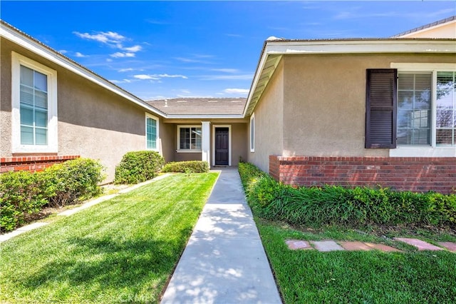 entrance to property featuring a lawn, stucco siding, and brick siding