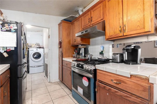 323 Whipple Mountain Rd, San Bernardino, CA 92410 - kitchen with brown cabinetry, light tile patterned floors, under cabinet range hood, washer / dryer, and stainless steel appliances