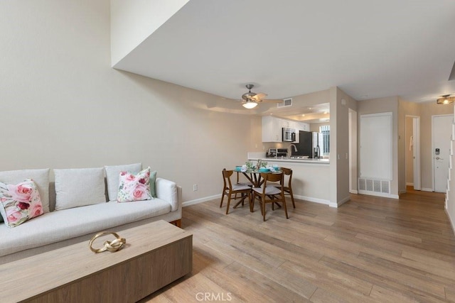 living area with a ceiling fan, baseboards, visible vents, and light wood finished floors