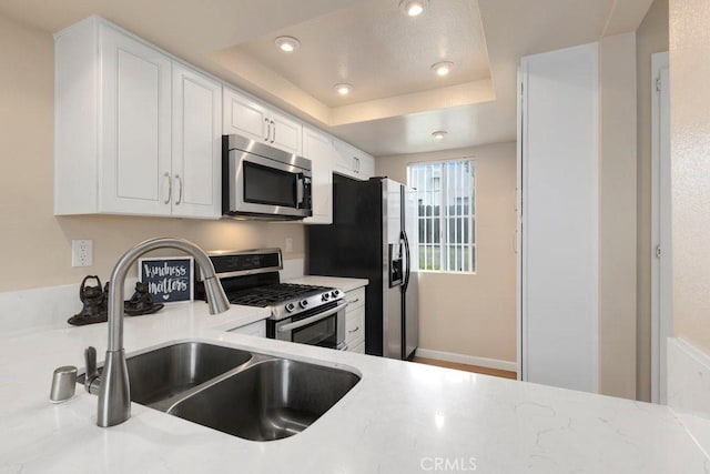 kitchen featuring recessed lighting, white cabinets, a tray ceiling, a sink, and appliances with stainless steel finishes