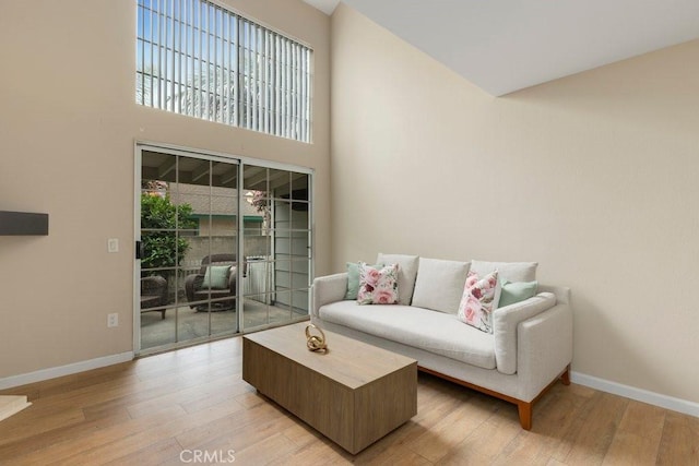 living area with light wood-type flooring, baseboards, and a high ceiling