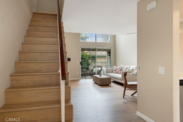 stairs with baseboards, wood finished floors, and a towering ceiling