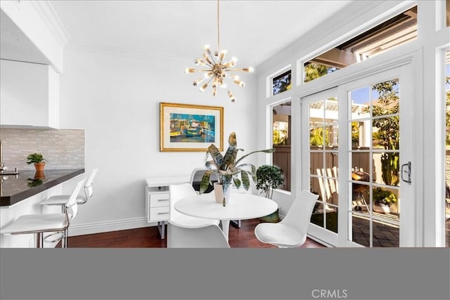dining room with dark wood finished floors, baseboards, ornamental molding, and an inviting chandelier