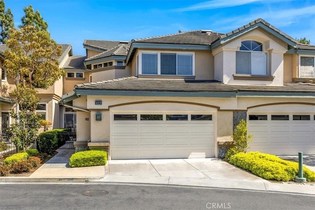 multi unit property with stucco siding, a tiled roof, driveway, and a garage