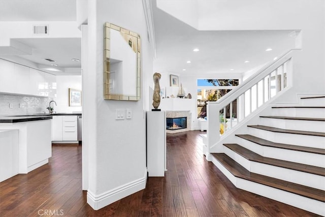 interior space featuring recessed lighting, stairs, a glass covered fireplace, dark wood-style floors, and visible vents