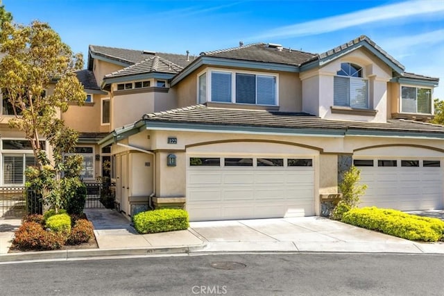 townhome / multi-family property with fence, concrete driveway, a tiled roof, an attached garage, and stucco siding