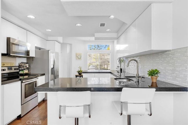 kitchen featuring white cabinetry, a sink, appliances with stainless steel finishes, visible vents, and a peninsula