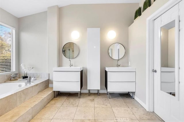 bathroom featuring tile patterned floors, two vanities, a bath, and a sink