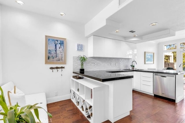 kitchen featuring stainless steel dishwasher, dark countertops, a sink, dark wood-style floors, and a peninsula