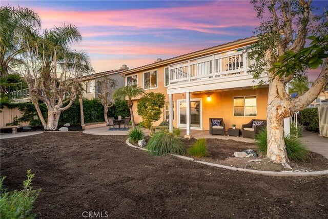 43 La Sordina, Rancho Santa Margarita, CA 92688 - back of property at dusk with a balcony, a patio, an outdoor living space, and stucco siding