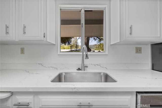 kitchen featuring white cabinets, light stone counters, and a sink
