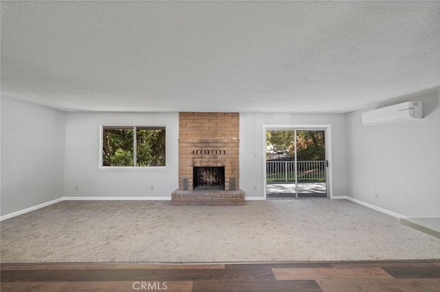 unfurnished living room with a brick fireplace, wood finished floors, baseboards, a textured ceiling, and a wall unit AC