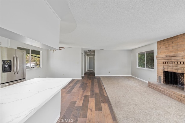 unfurnished living room with a textured ceiling, a brick fireplace, a wealth of natural light, and dark wood-style floors