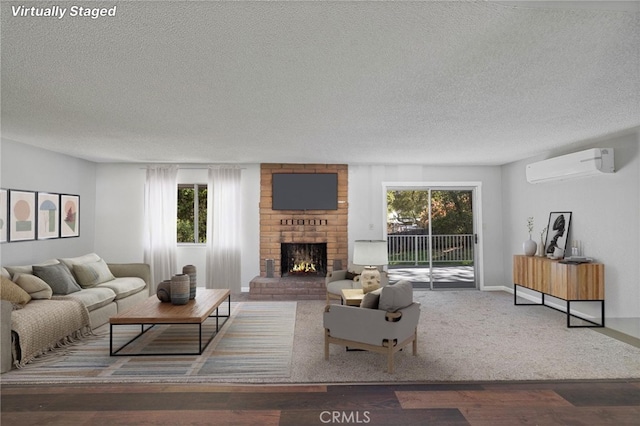 living area with wood finished floors, a textured ceiling, a brick fireplace, and a wall unit AC