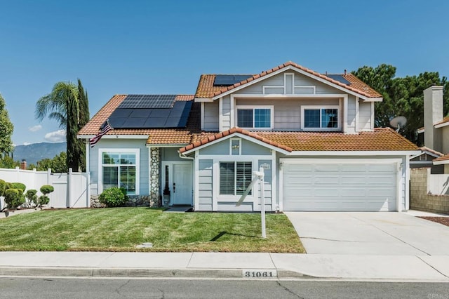 view of front of house featuring fence, a tile roof, a front yard, roof mounted solar panels, and driveway