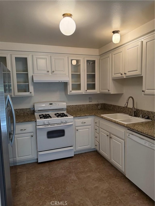 kitchen with dark countertops, a sink, white appliances, white cabinets, and under cabinet range hood