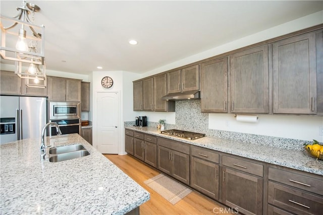 11534 Alana Ln, Beaumont, CA 92223 - kitchen featuring under cabinet range hood, stainless steel appliances, a sink, decorative light fixtures, and light wood-style flooring