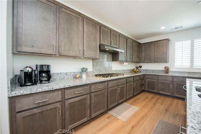 11534 Alana Ln, Beaumont, CA 92223 - kitchen featuring stainless steel gas cooktop, dark brown cabinetry, light wood-style flooring, under cabinet range hood, and visible vents