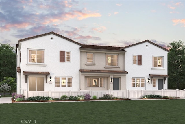 back of house at dusk featuring stucco siding, a lawn, and a fenced front yard