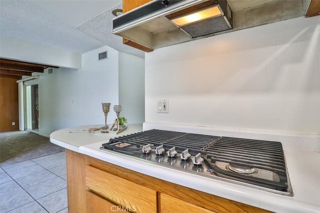 kitchen featuring visible vents, light countertops, under cabinet range hood, light tile patterned floors, and stainless steel gas stovetop