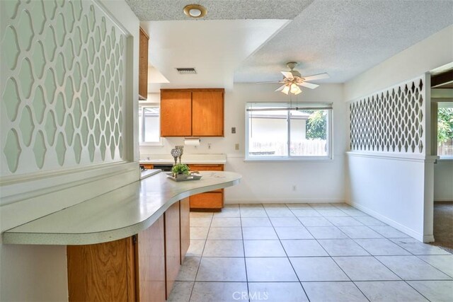 kitchen with brown cabinetry, light countertops, plenty of natural light, and a ceiling fan