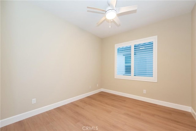spare room featuring light wood finished floors, a ceiling fan, and baseboards